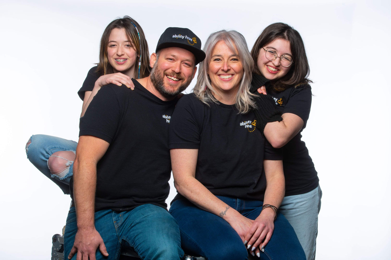 Four people wearing black shirts with a logo, sitting together on a white background
